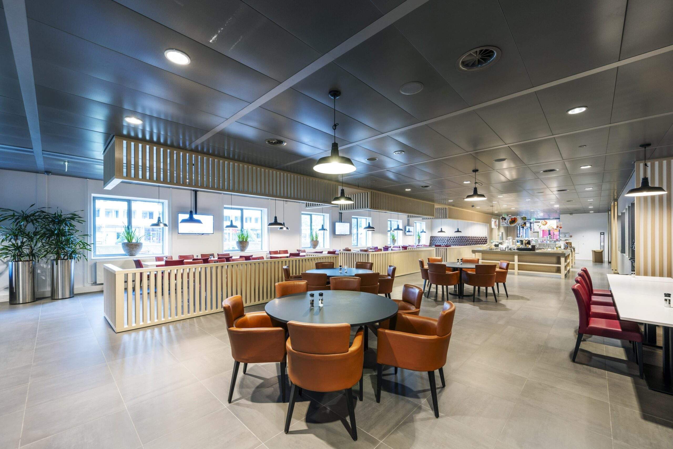 Modern bedrijfsrestaurant aan het Koningin Wilhelminaplein met ronde en rechte tafels, leren stoelen en een open buffetruimte.